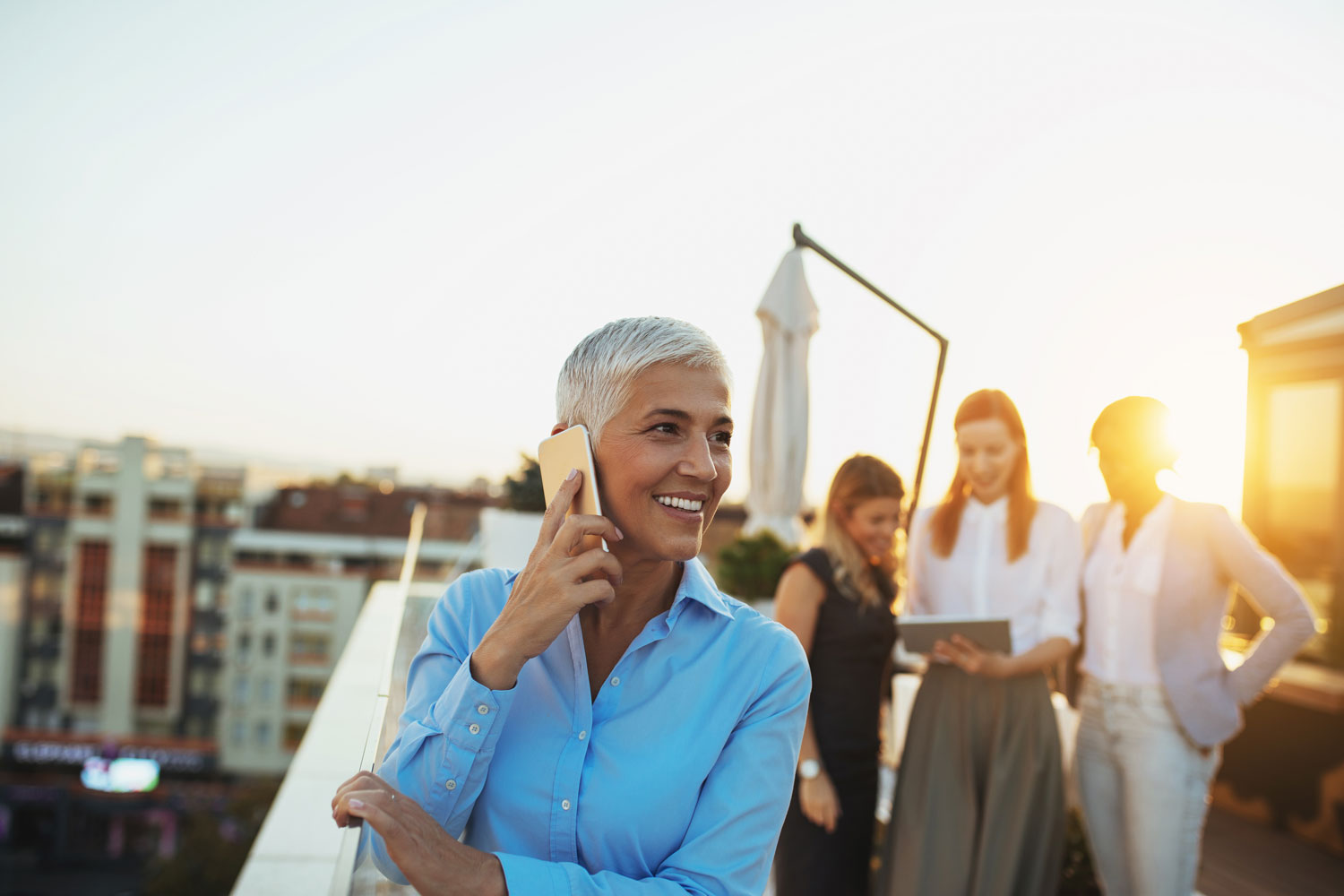 Smiling mature woman on phone with colleagues in background.